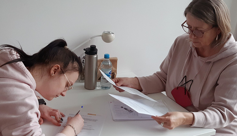 Elisabeth Eberl sitzt mit einer Jugendlichen an einem Tisch. Sie füllen gemeinsam Formulare aus.