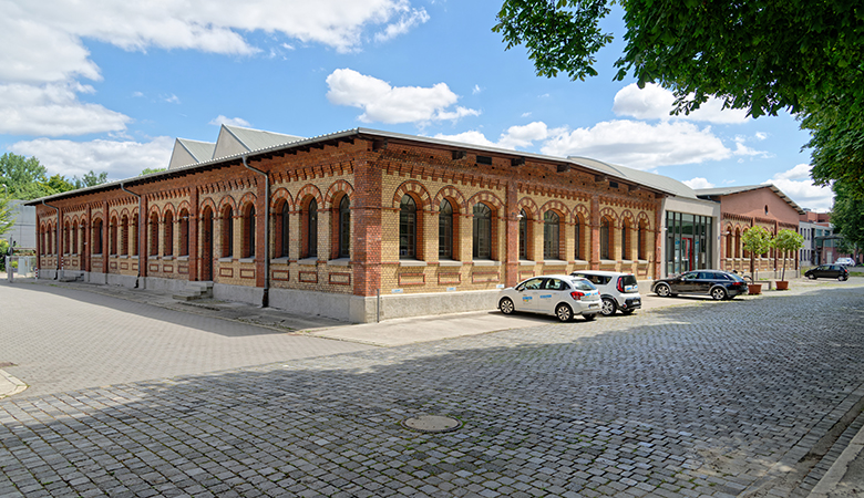 Das Gebäude der infau-lern/statt GmbH. Davor befindet sich ein großer gepflasterter Parkplatz mit geparkten Autos.