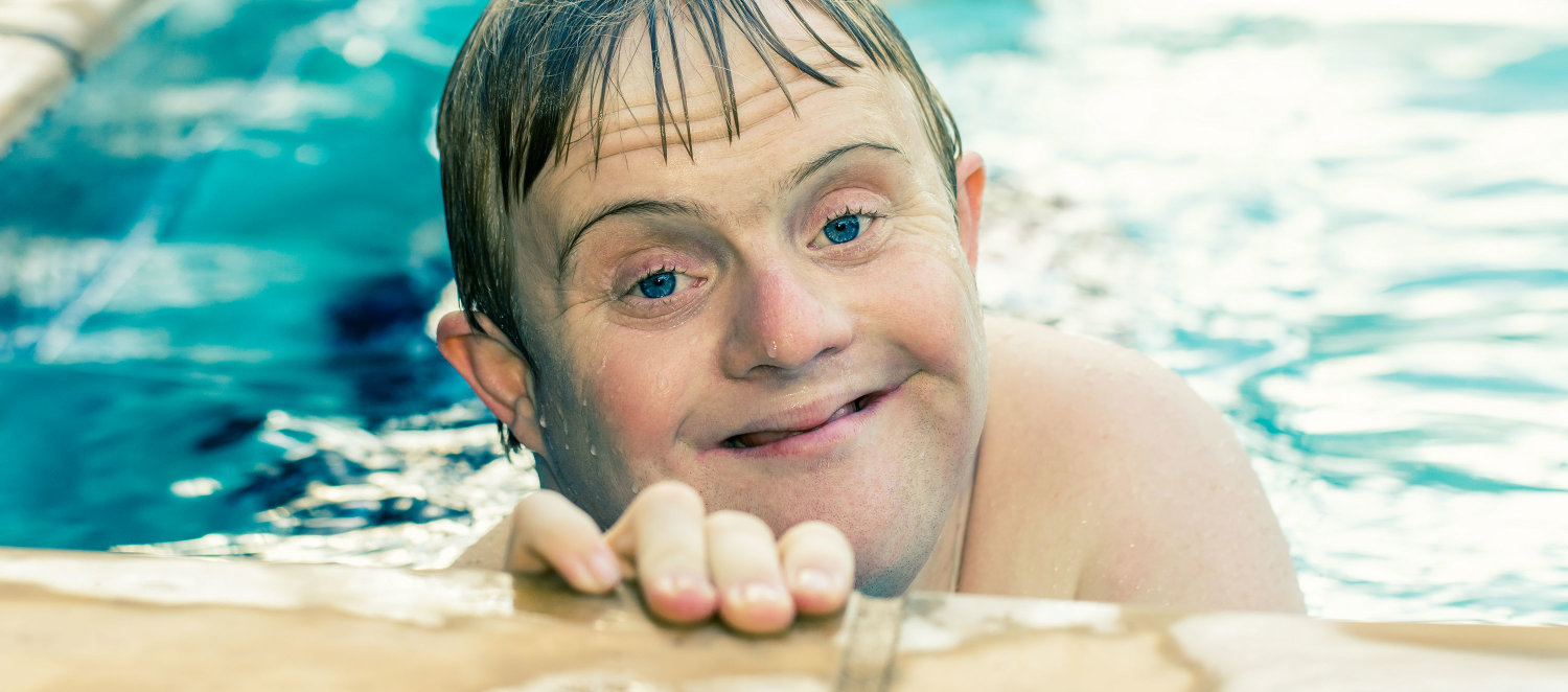 Im Schwimmbad: Ein junger Mann mit Down-Syndrom guckt lächelnd aus dem Becken.
