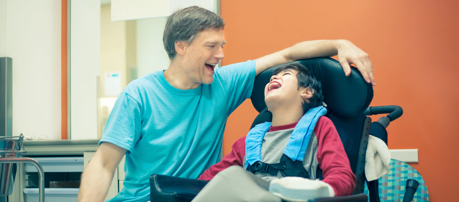 Eine Fachkraft und ein Junge mit Rollstuhl lachen zusammen.