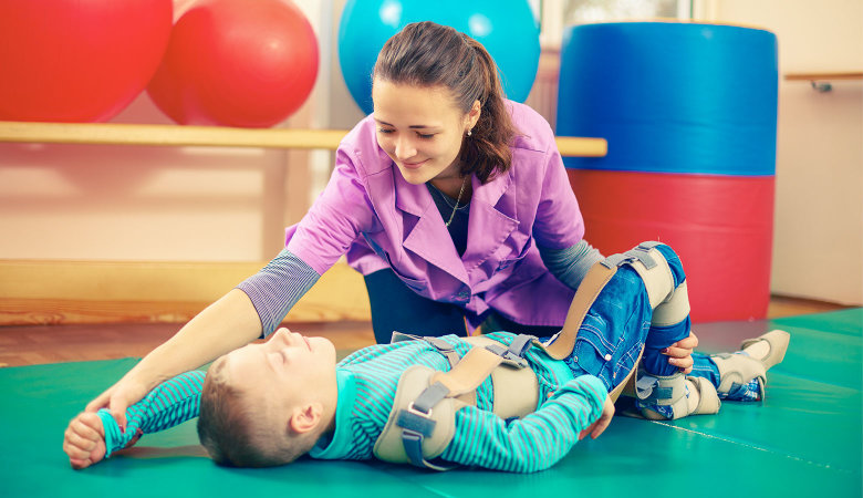 Im Therapieraum: Eine Fachkraft macht mit einem Jungen Übungen auf der Matte.