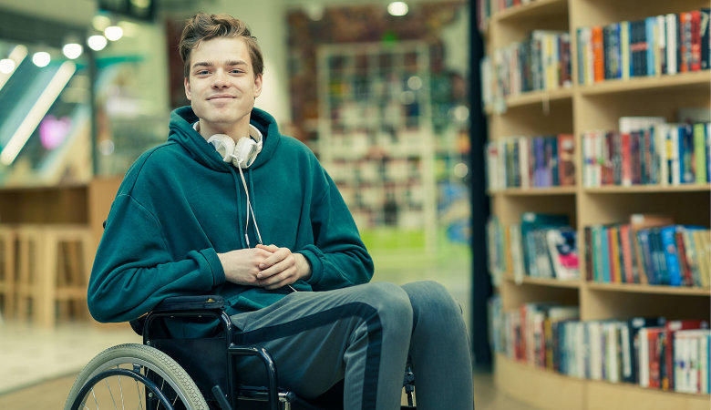 Ein Junge sitzt im Rollstuhl in einer Bücherei.