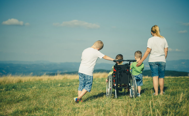 Eine Frau steht auf einer Wiese und genießt zusammen mit drei Kindern die Aussicht. Ein Kind sitzt im Rollstuhl.