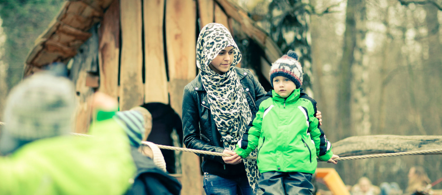 Szene im Kindergarten: Eine Frau mit Kopftuch spielt mit Kindern im Garten.