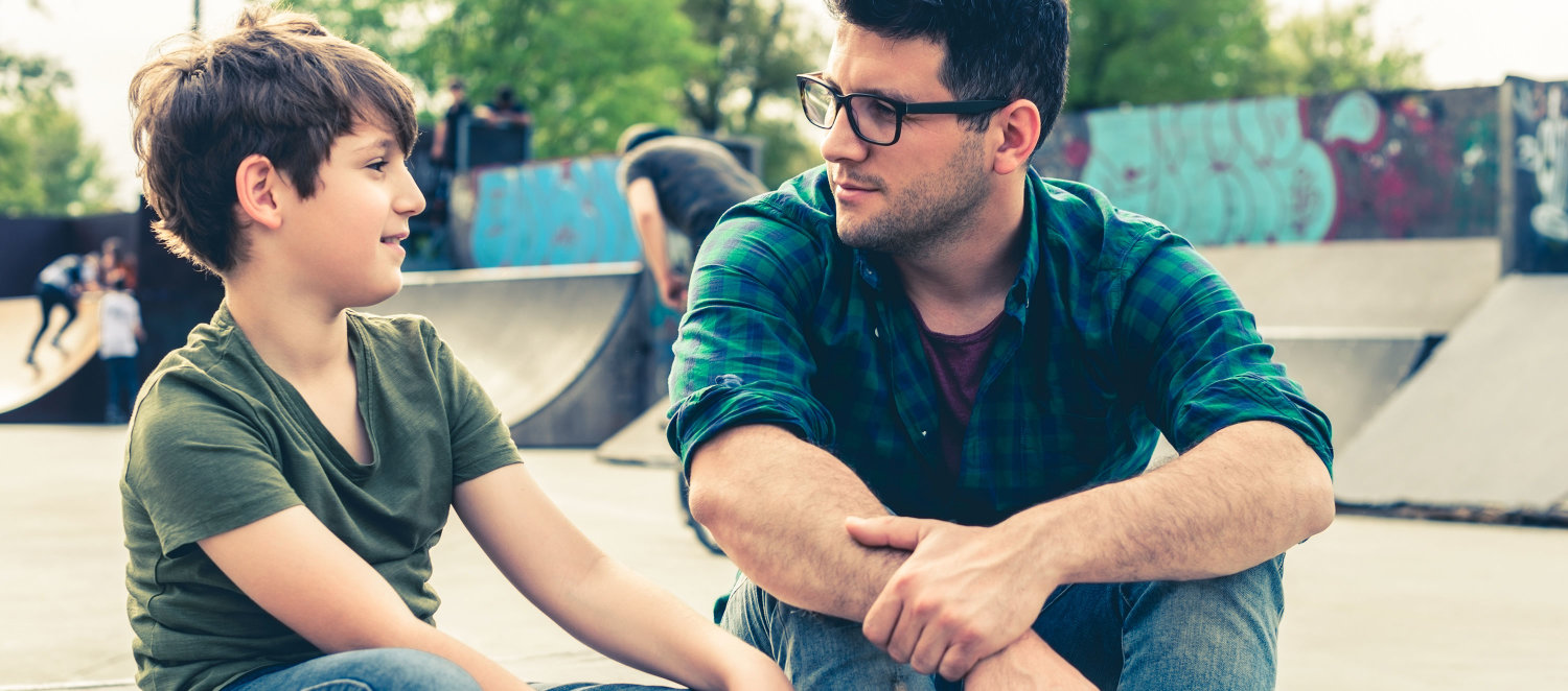 Ein Mann und ein Junge sitzen zusammen auf einer Rampe im Skatepark und führen ein Gespräch. 
