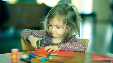 Ein kleines Mädchen schneidet sehr konzentriert mit einer Schere einen Bastelbogen.