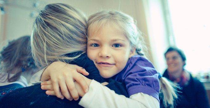 Ein kleines Mädchen auf dem Arm einer Betreuerin lächelt pfiffig in die Kamera. 