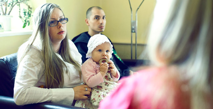 In einer Beratungsstelle: Ein junges Paar mit Baby sitzt auf einem Sofa.