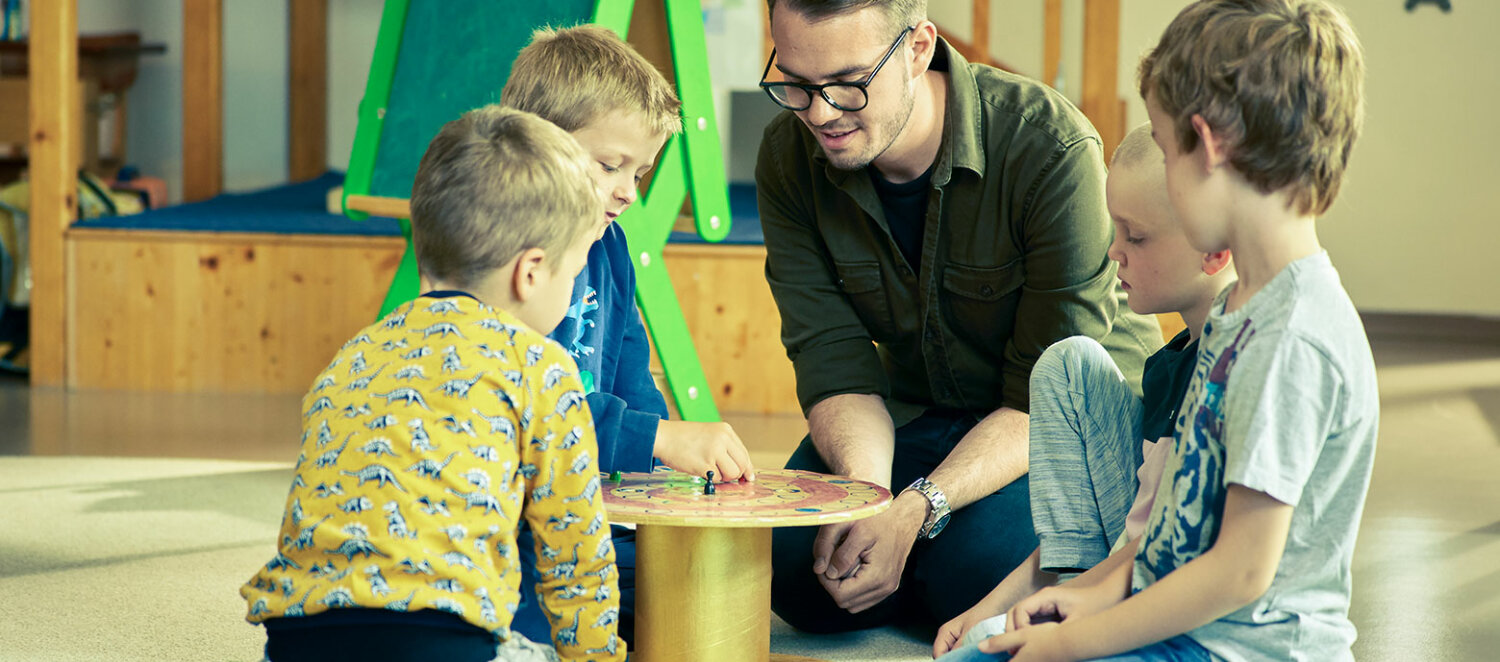 Vier Kinder spielen mit ihrem Erzieher ein Brettspiel