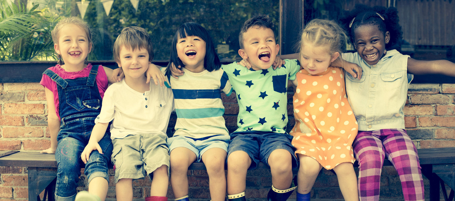 Szene aus dem Kindergarten: Lachende Kinder mit Gummistiefeln sitzen nebeneinander auf einer Bank.
