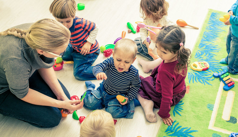 Szene im Kindergarten: Eine Erzieherin schlichtet Streit zwischen kleinen Kindern.