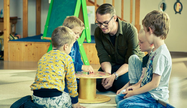 Szene im Kindergarten: Erzieher spielt mit drei Jungen ein Brettspiel.