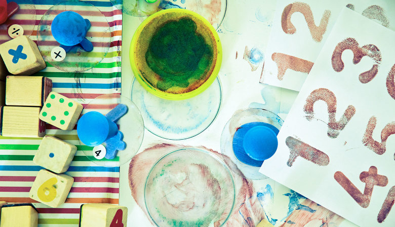 Szene im Kindergarten: Nahaufnahme eines Basteltischs mit Farben, Papieren und Stempeln.